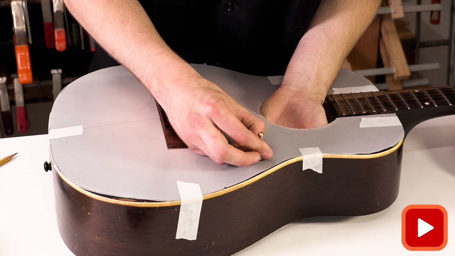Hands attaching tracing paper to acoustic guitar top